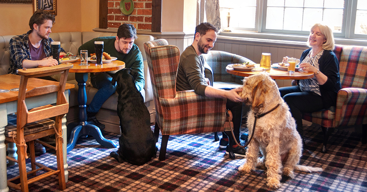 men and women eating food inside The Kingslodge Inn with two dogs sat at their feet.